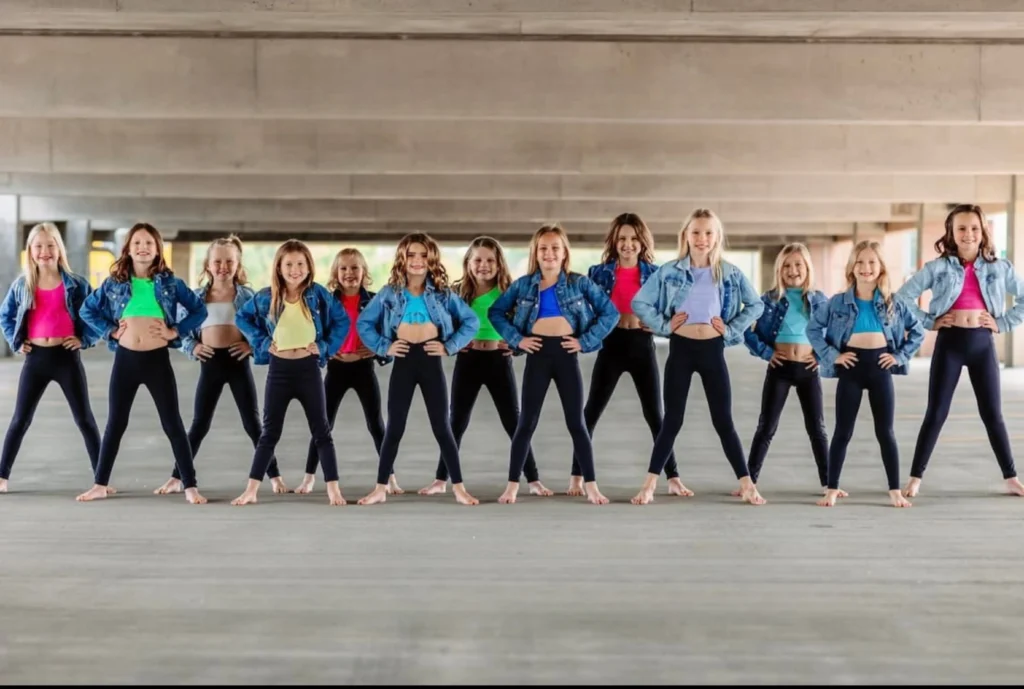 Child dancers lined up wearing colorful tops with black leggings